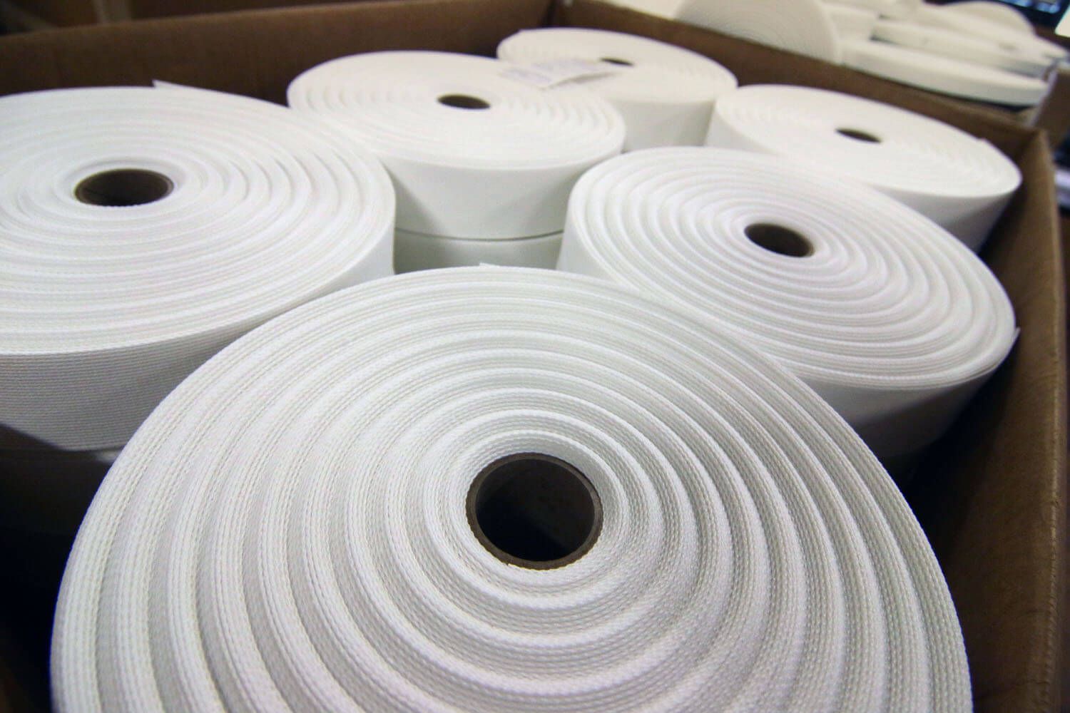 Close up of several rolls of white fabric sitting in a cardboard box