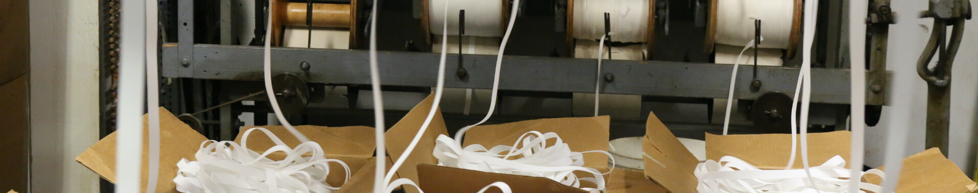 Bleached white fabric exiting a manufacturing process and collecting in cardboard boxes