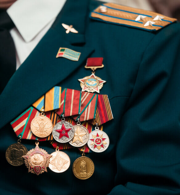 The upper left chest of a dark green military jacket covered by many military award pins.