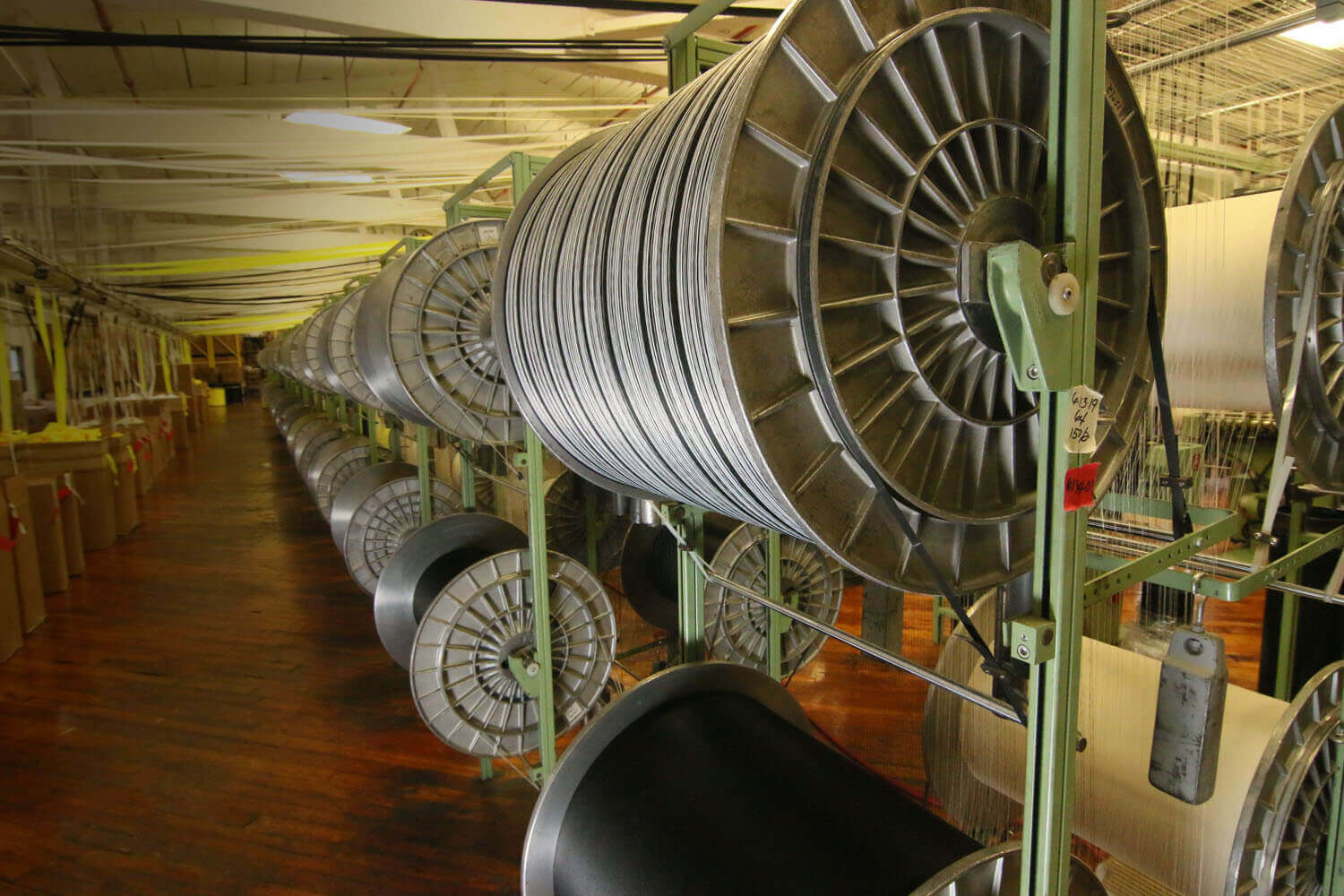 Dozens of giant empty fabric roll holders being stored on shelves inside of a textile mill