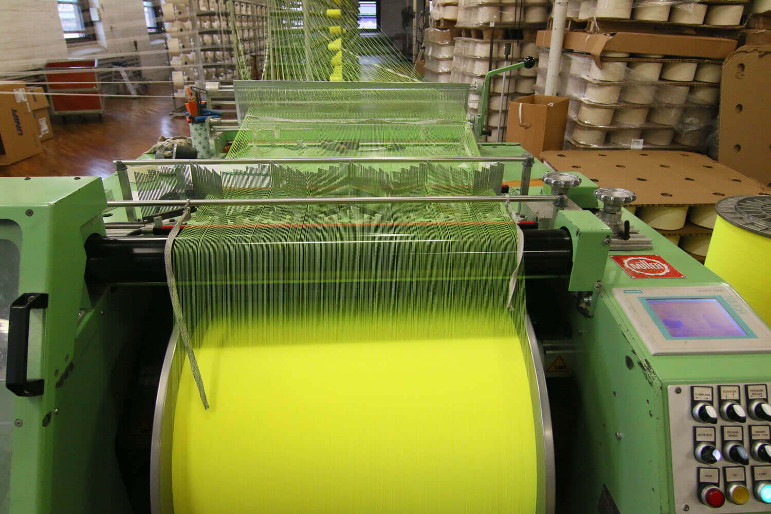 Strands of yellow fabric being rolled together at the end of the textile manufacturing process