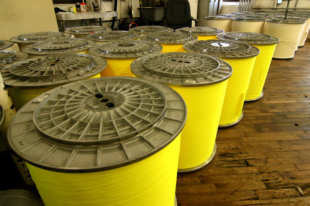 Dozens of large rolls of yellow and tan fabric sitting inside of a textile facility
