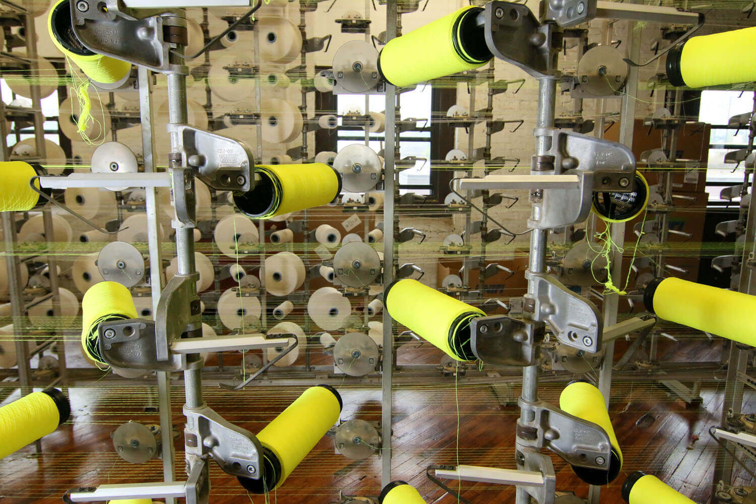 Several small rolls of yellow and white fabric being processed by a tall metal piece of machinery