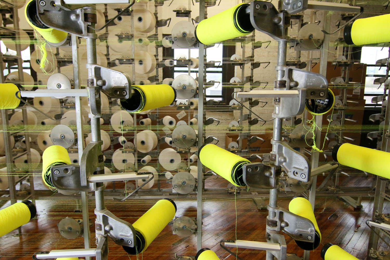 Several small rolls of yellow and white fabric being processed by a tall metal piece of machinery