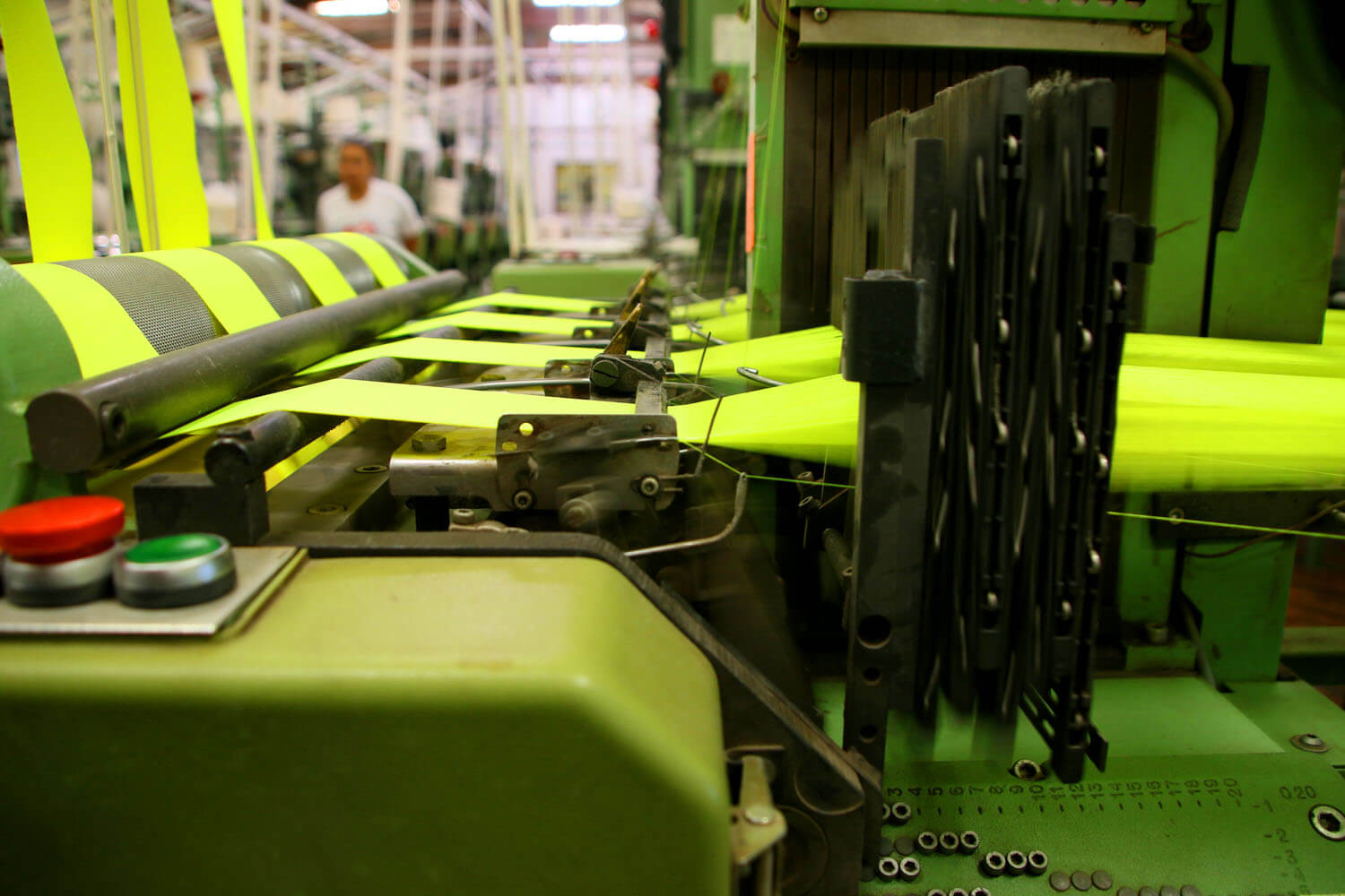 A machine in a textile mill manufacturing large pieces of yellow fabric with an employee in the background