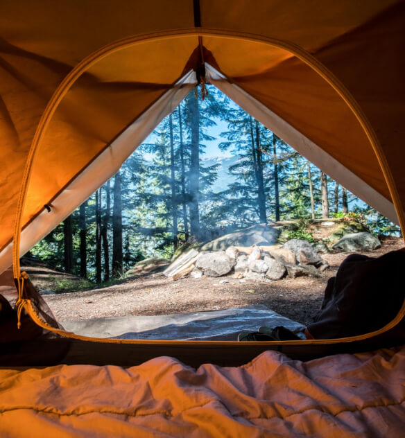View looking out through the entrance of an orange camping tent outside in a sunny forest